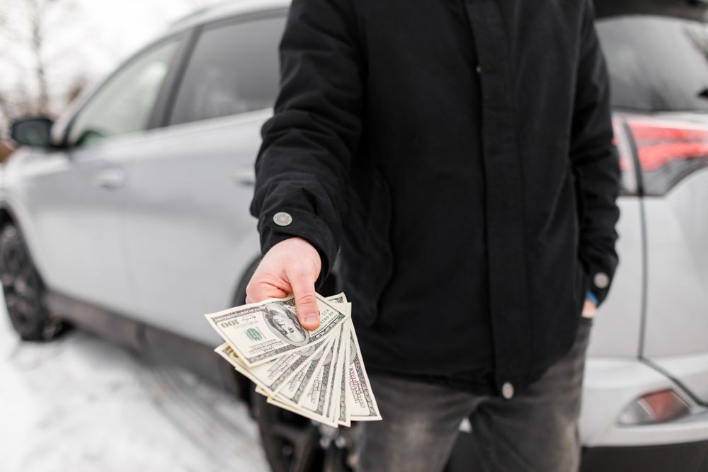 Man holding cash in front of a car